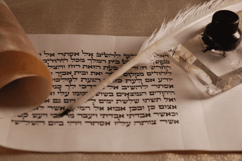 A piece of paper with some Hebrew writing, a quill, and an ink bottle.