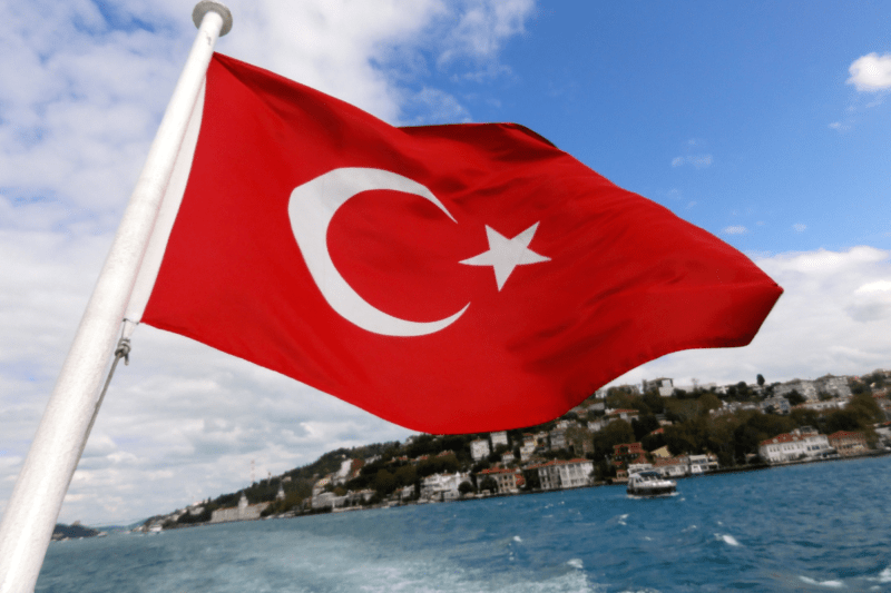 The flag of Turkey on the back of a boat with an island in the background